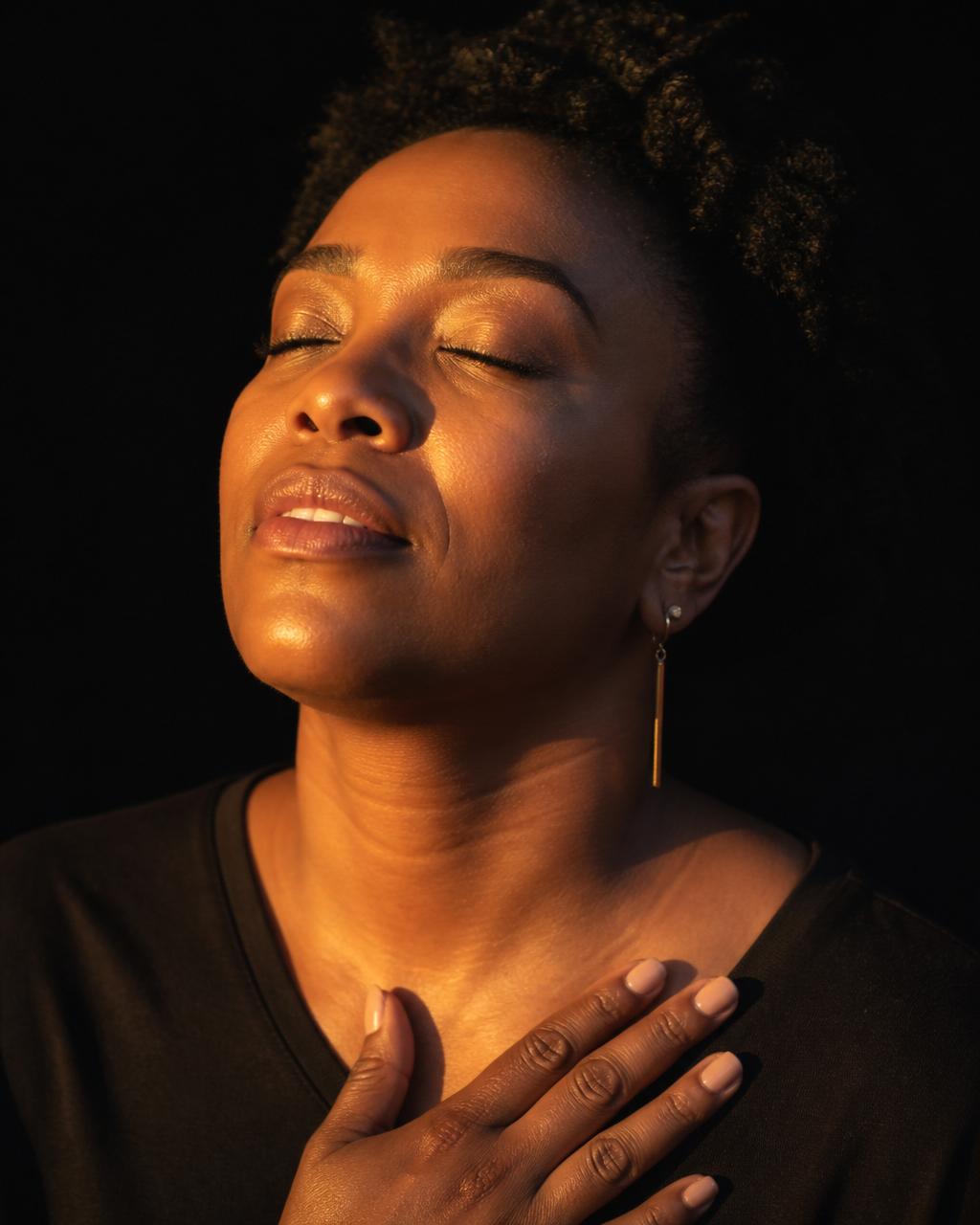 A woman in prayer at dawn, hand on chest, lit by warm golden light
